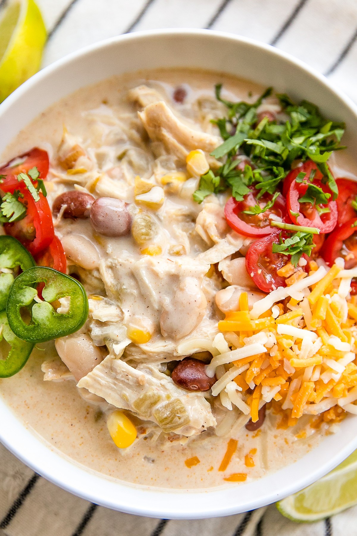 A bowl of chicken chili with shredded cheese and other toppings.