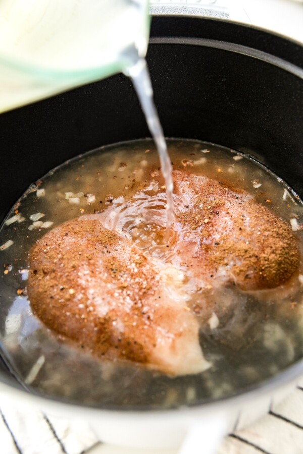Pouring broth over chicken breasts.