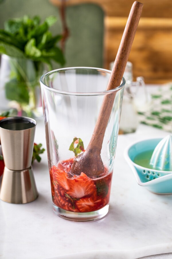 Strawberries, mint, and simple syrup in a tall glass with a muddle.