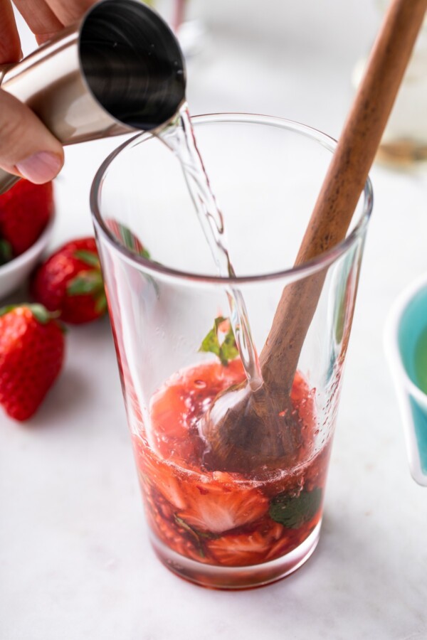 Pouring white rum over muddled strawberries and mint.