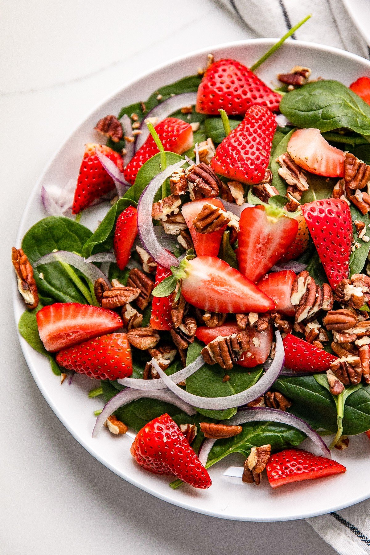 Overhead shot of a spinach strawberry salad made with red onions and pecans.