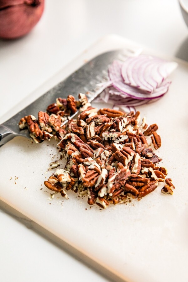 Chopped pecans and sliced red onion on a cutting board.