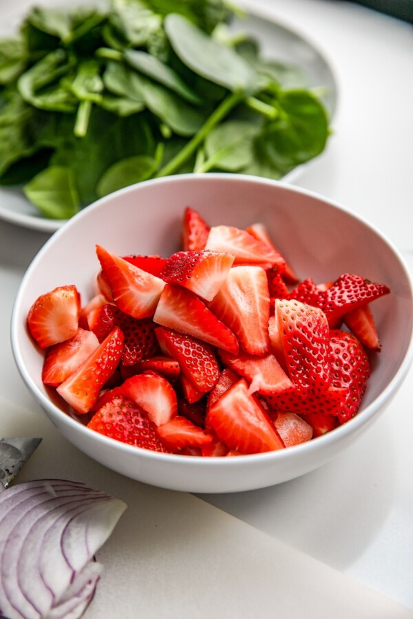 Hulled and quartered strawberries in a white bowl.