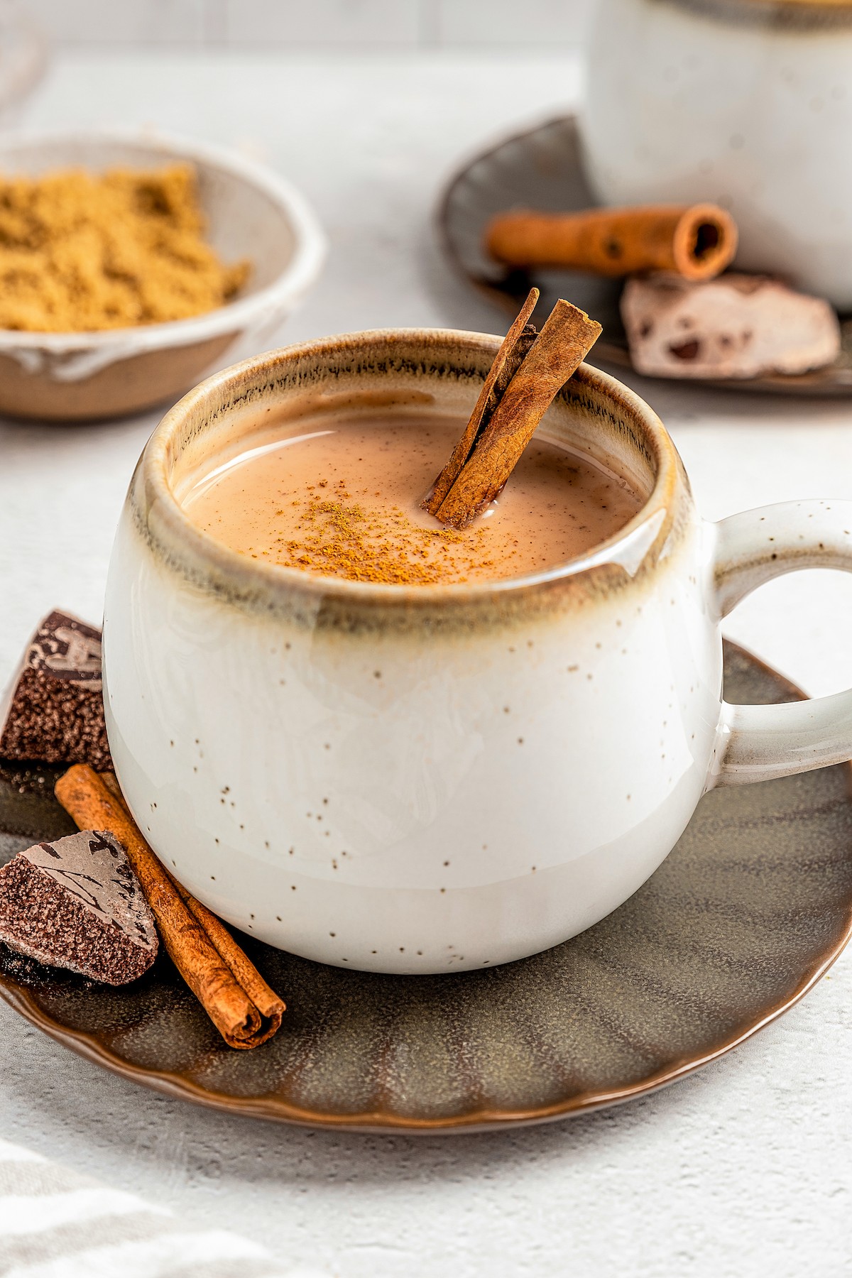 A mug of Chocolate Atole with cinnamon sticks and Mexican chocolate on the side.