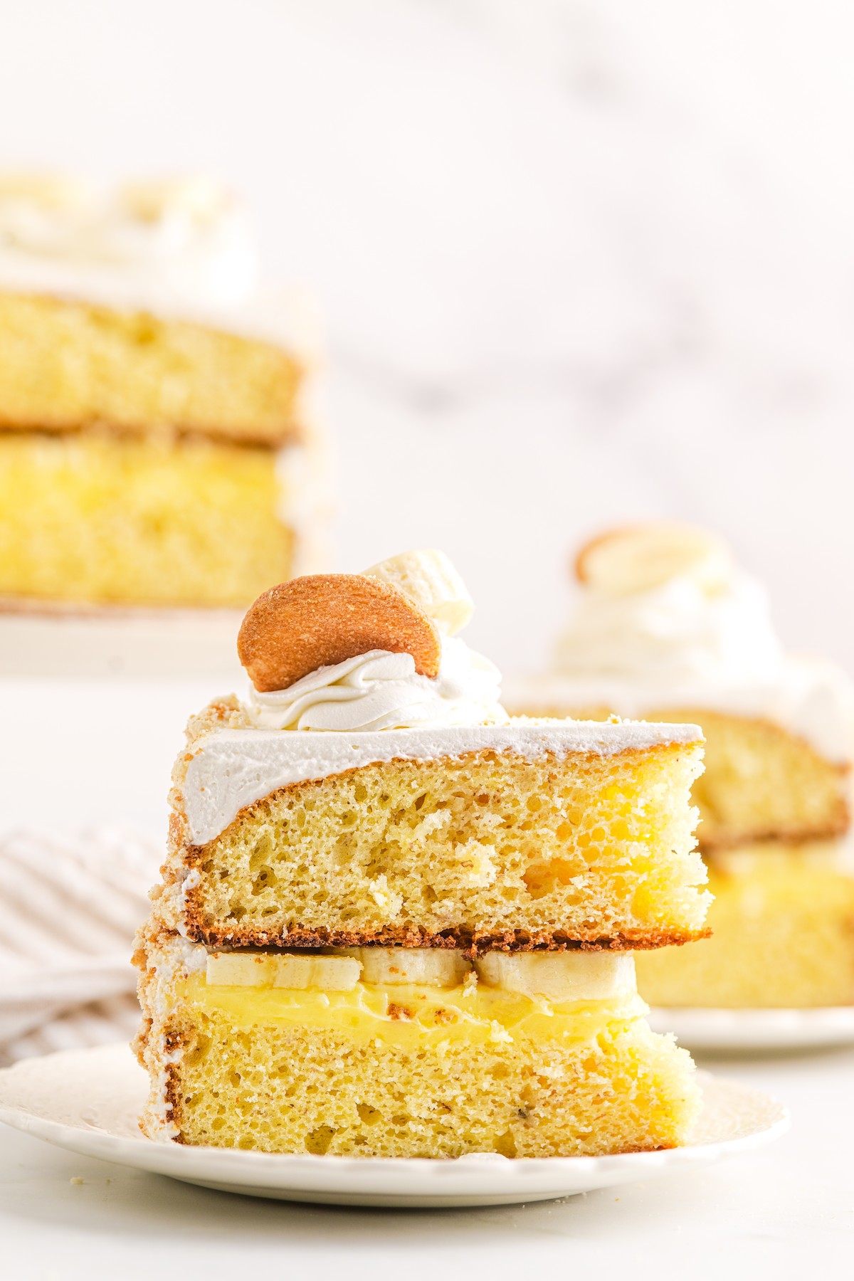 Side view of a slice of banana pudding cake, showing the layers of cake, pudding, bananas, and whipped cream.