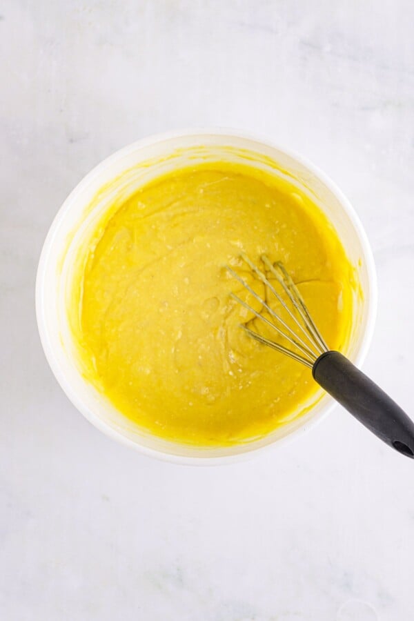 Yellow cake batter in a bowl with a whisk.