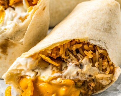 Close-up of half a burrito, cut on the diagonal with cheese and chips spilling out.