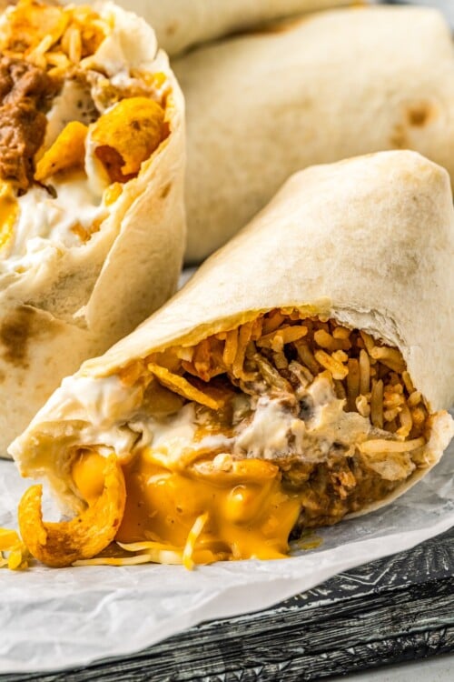 Close-up of half a burrito, cut on the diagonal with cheese and chips spilling out.