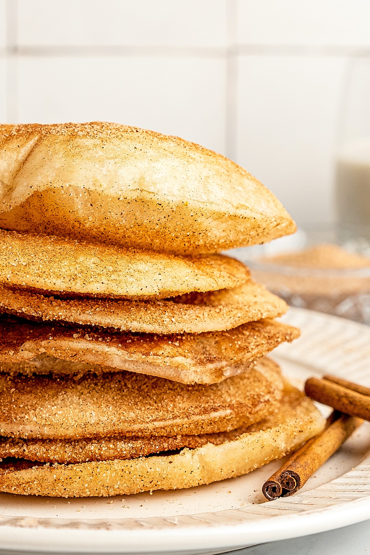 Buñuelos stacked on a plate with a cinnamon stick.
