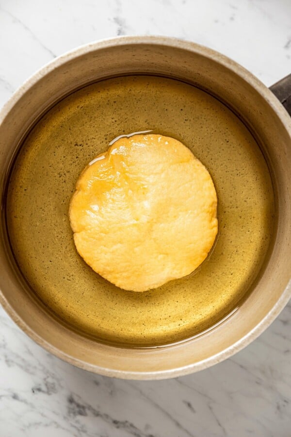 A flour tortilla being fried in a pot of oil.