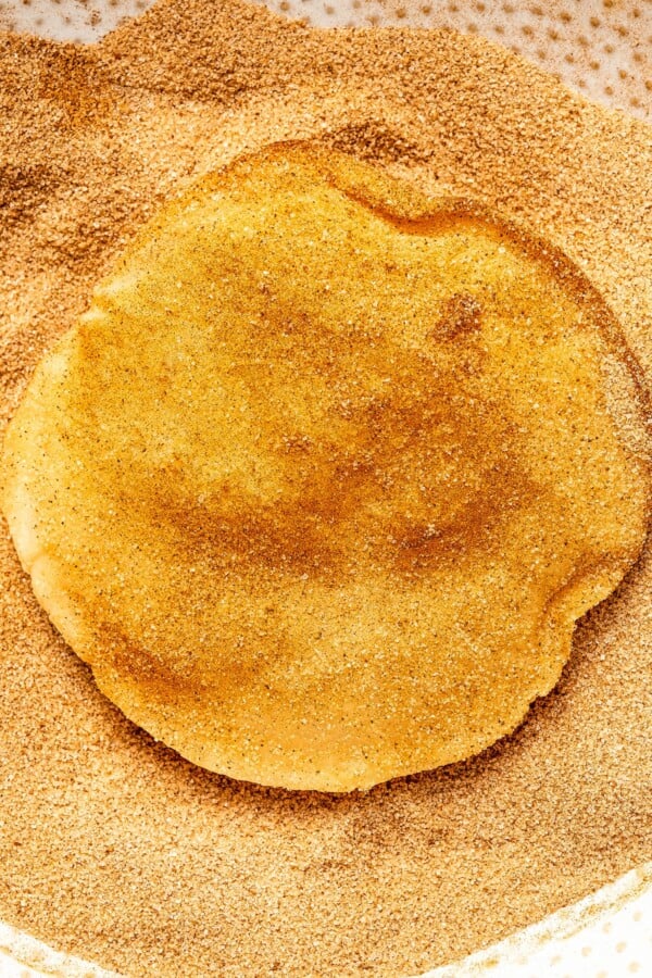 A fried flour tortilla being coated in cinnamon sugar.