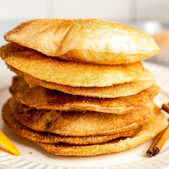 A stack of buñuelos on a plate with cinnamon sticks and orange peel.