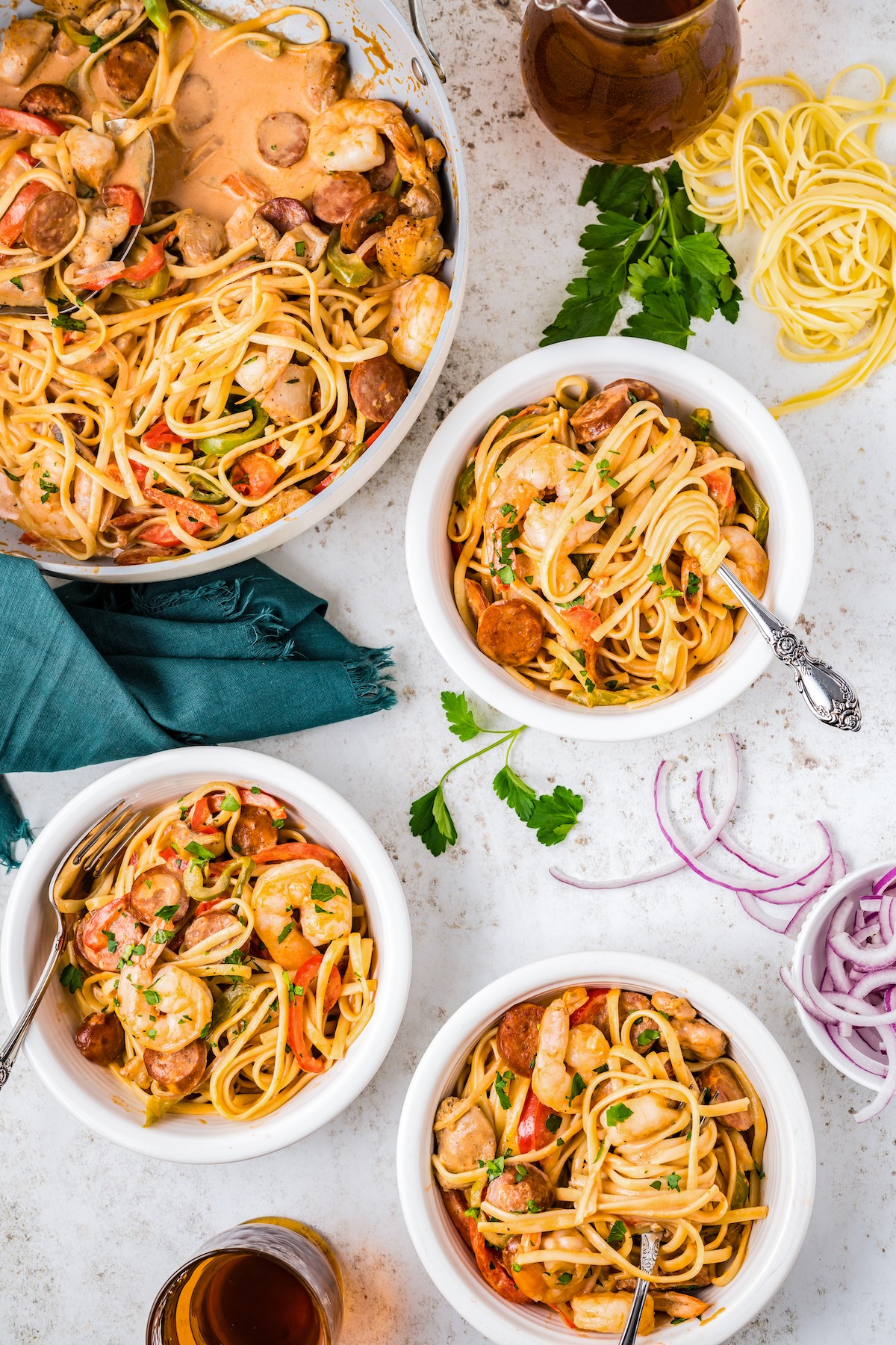 Three bowls of Cajun Jambalaya Pasta with forks and a skillet filled with jambalaya pasta.