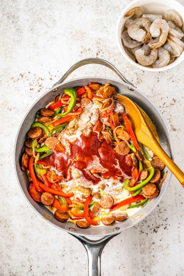 Heavy cream, tomato sauce and more in a skillet with sausage, bell peppers, onions and garlic.