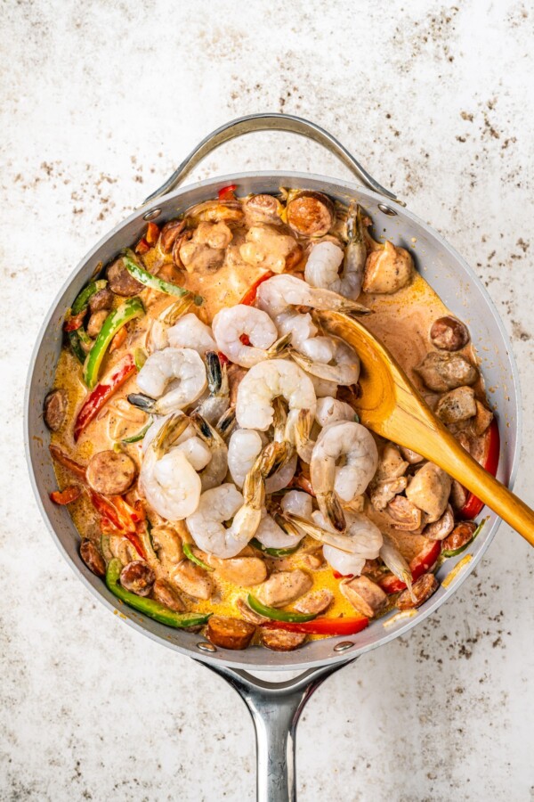 Shrimp being added to a skillet with bell peppers, sausage, onions and sauce.