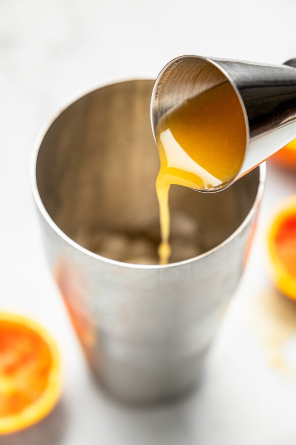 Fresh orange juice being poured into a cocktail shaker.