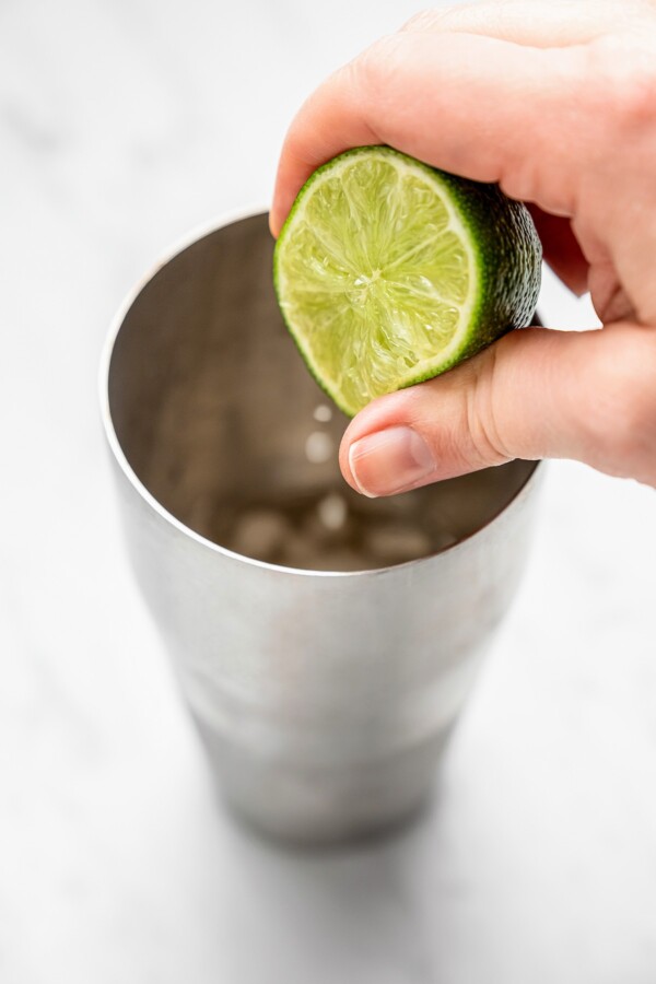 A lime being squeezed into a cocktail shaker.