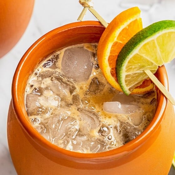 A clay mug filled with Mexican Cantaritos cocktail with lime and orange garnish on a skewer.