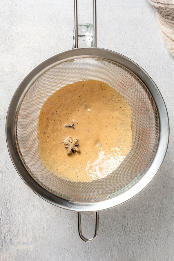 Draining spices with a strainer out of the evaporated milk and seasoning mixture.