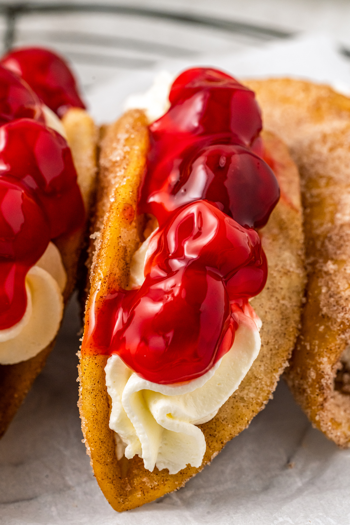 Cinnamon sugar dessert tacos are filled with cheesecake filling and topped with cherry pie filling.