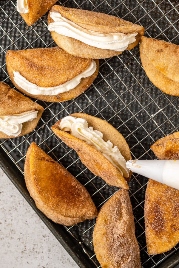 Fried tortillas coated in cinnamon sugar with cheesecake filling being piped into the shell with a piping bag.