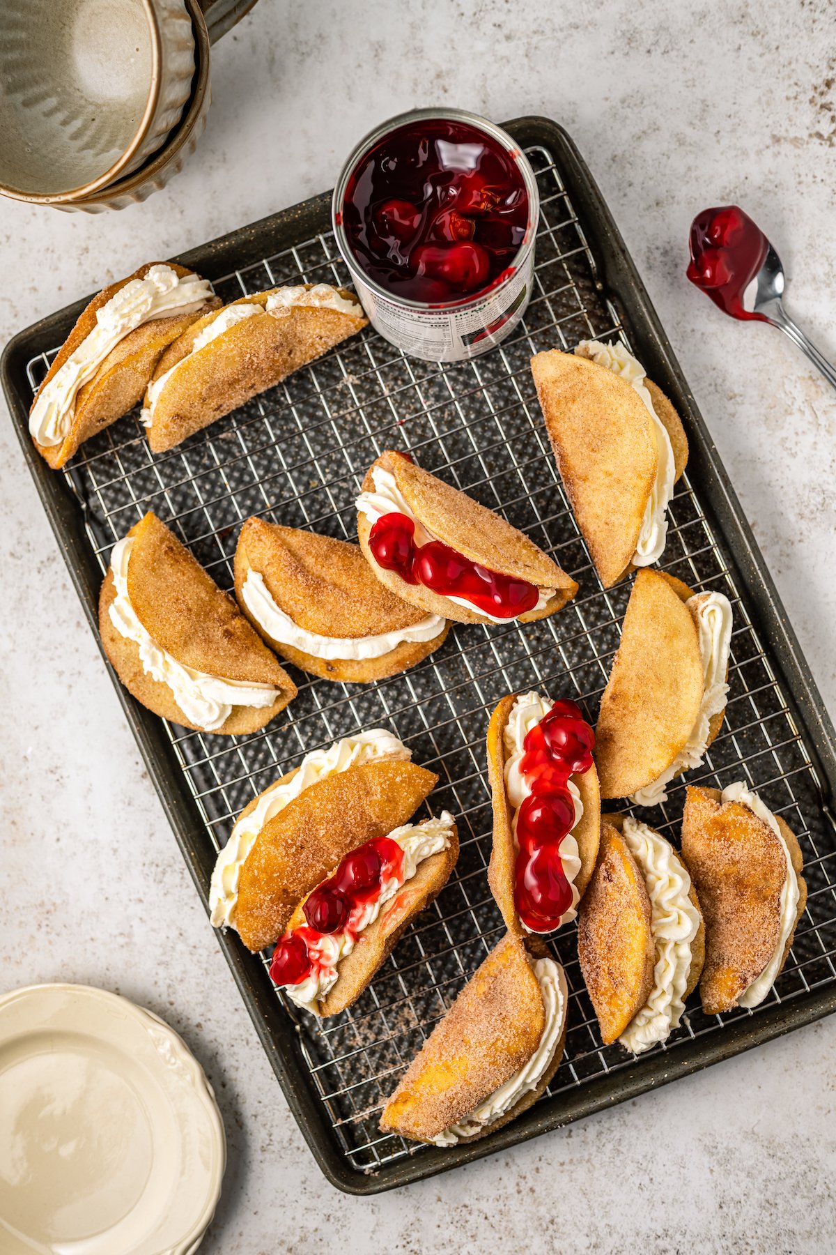 Cheesecake stuffed taco shells being topped with cherry pie filling.