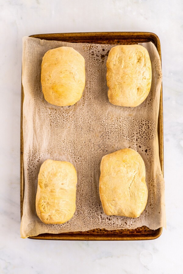 Baked ciabatta rolls on a parchment-lined baking sheet.
