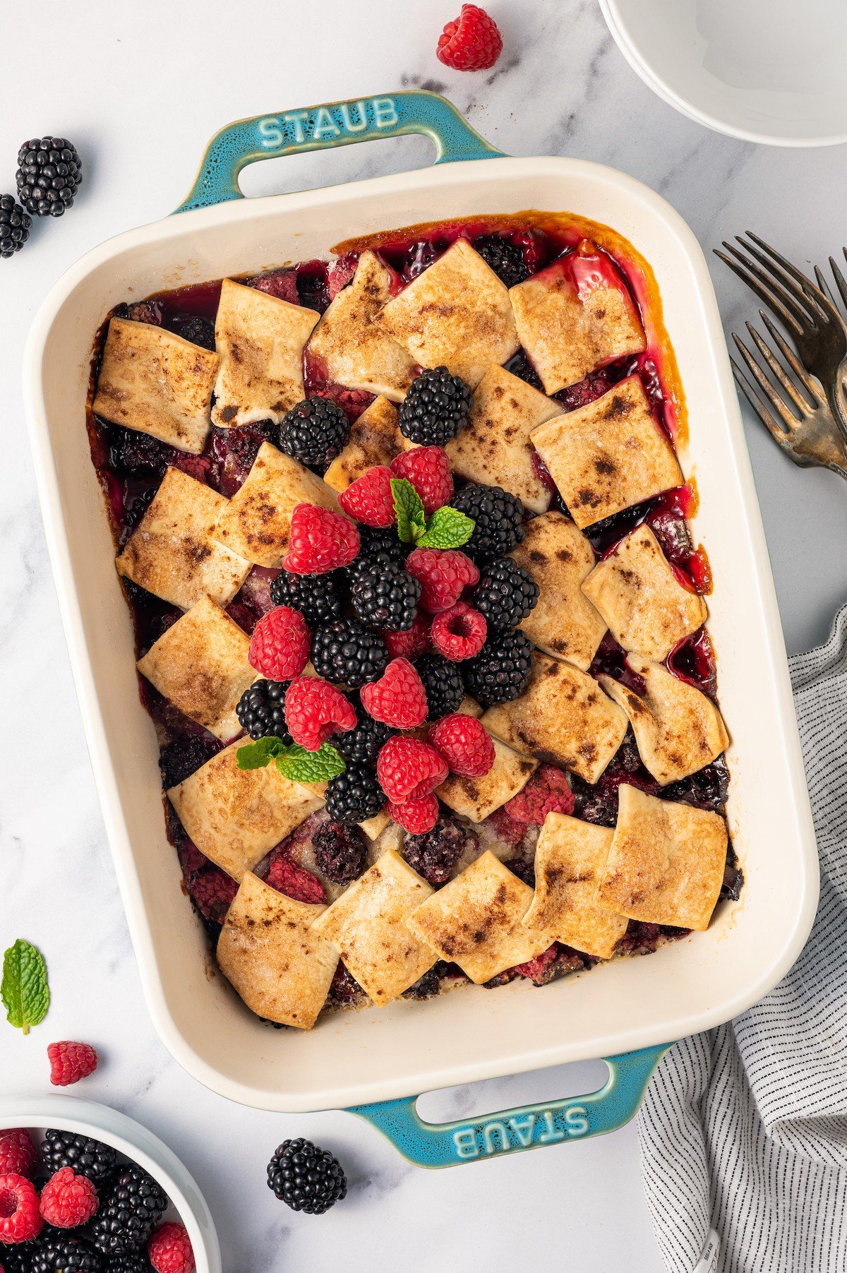Cooked berry cobbler in a casserole dish with fresh berries on top.