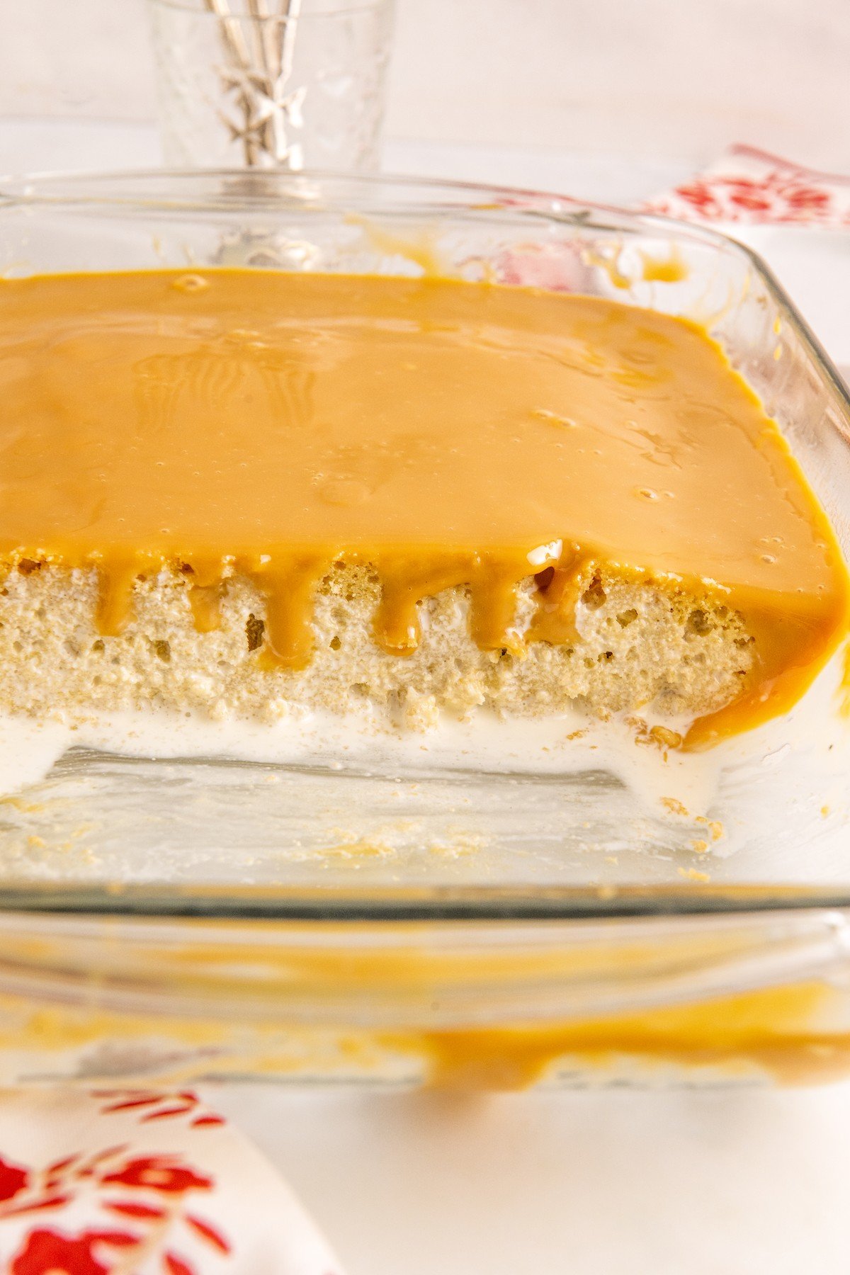 A cake made in a glass pan, with some slices cut out to show the sweetened condensed milk soaking the cake crumb and the topping drizzling down the sides.