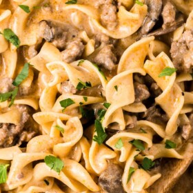 Easy Ground Beef Stroganoff in a skillet with fresh herbs on top and a wooden spoon scooping up a serving.