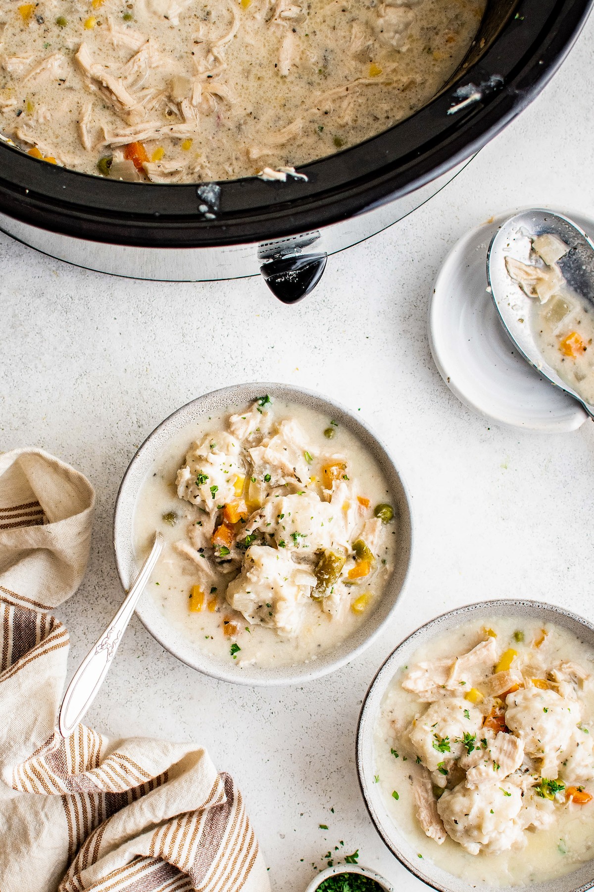 Bowls of creamy chicken and biscuit dumplings next to a slow cooker.