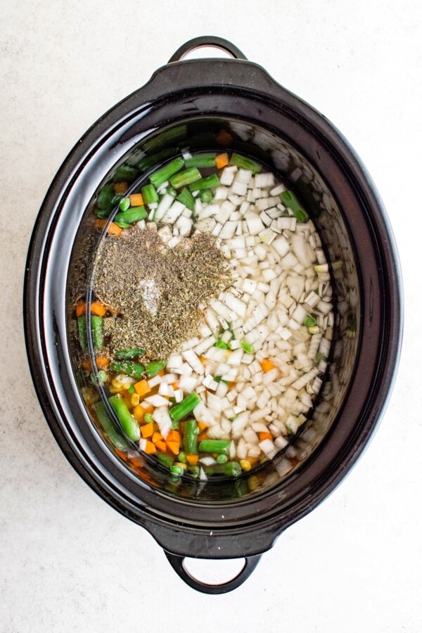Seasonings, vegetables, broth, and other ingredients in a slow cooker.