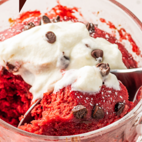 A spoon scooping up a bite of red velvet mug cake out of a mug.