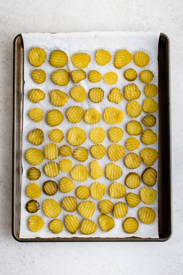 Dill chips laid in a single layer on a paper-towel-lined baking sheet.