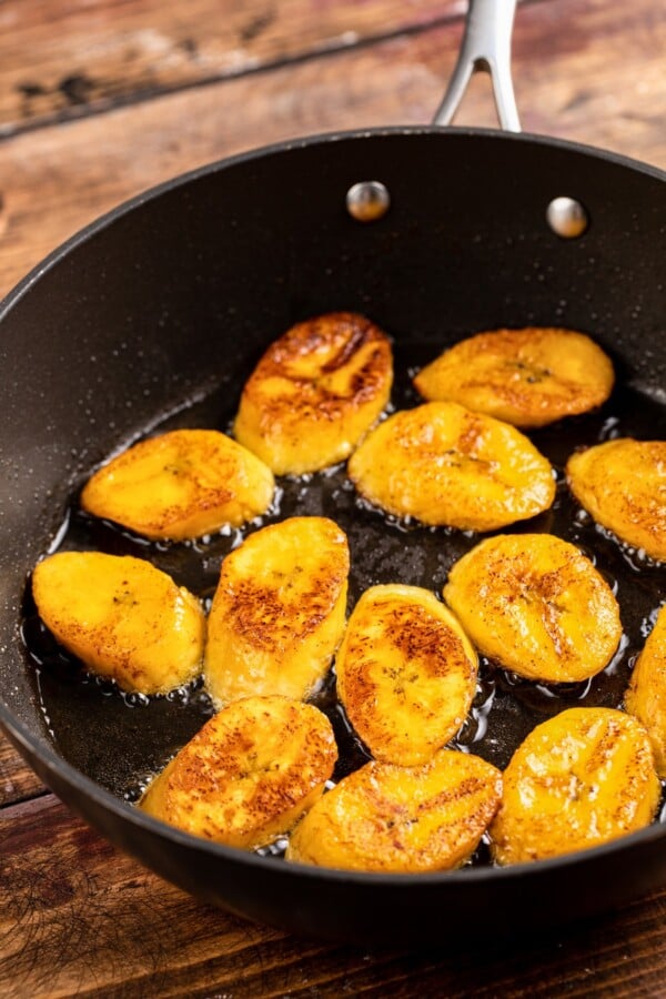 Plantains being fried in a skillet with butter.