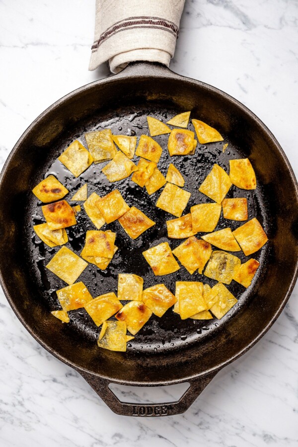 Corn tortillas being fried in oil in a cast iron skillet.