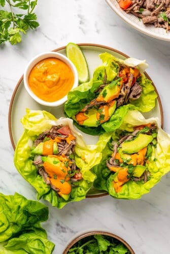 Salpicon wrapped in lettuce with fresh avocado on a plate with homemade chile sauce drizzled on top.