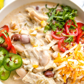 A bowl of white chili with jalapenos, shredded cheese, tomatoes and cilantro on top.