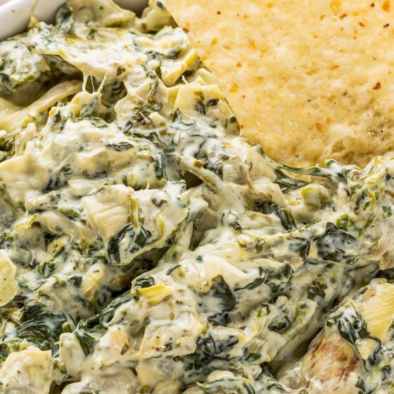A bowl of spinach artichoke dip with a tortilla chip in the dip.