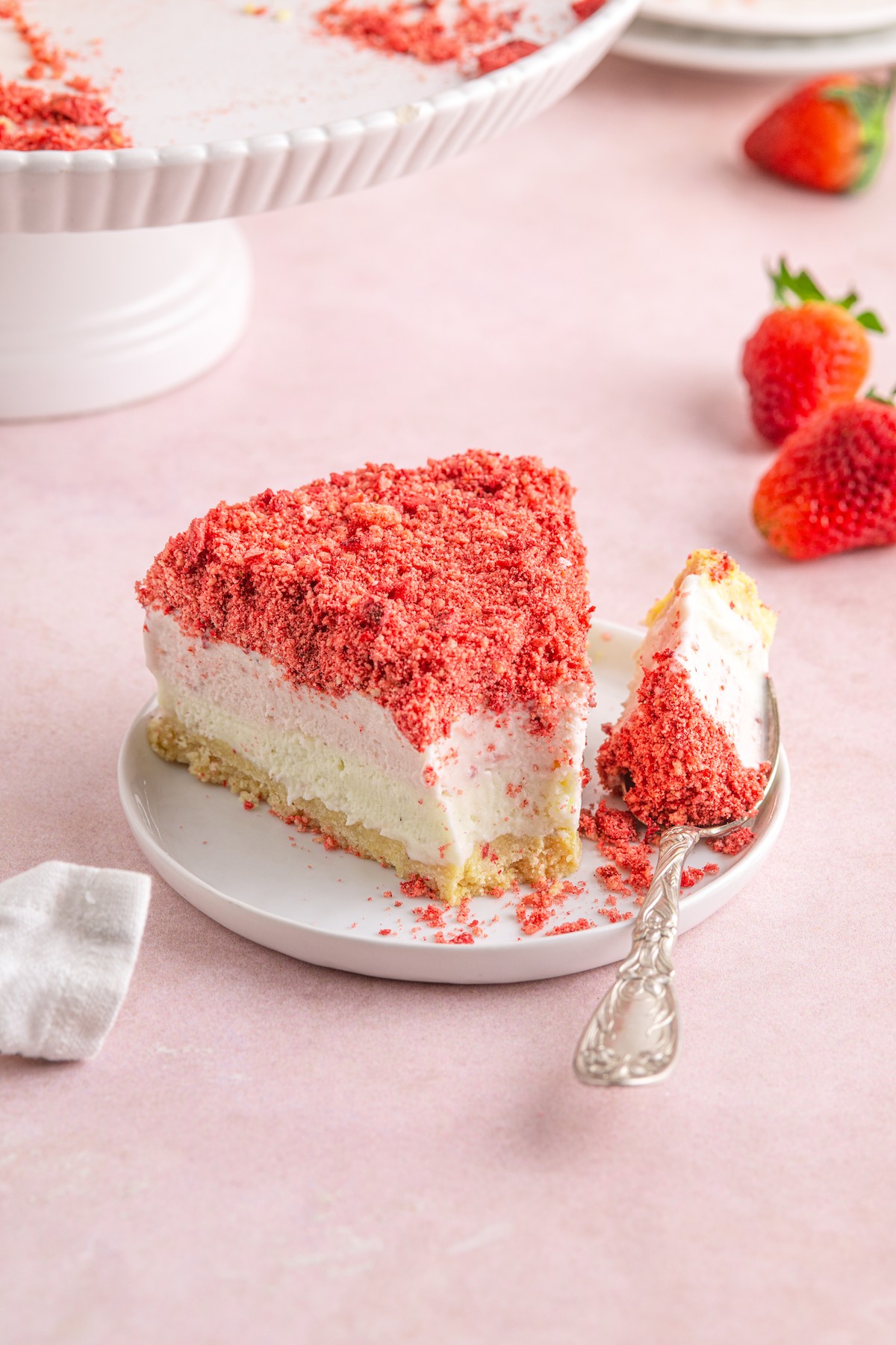 A wedge of strawberry shortcake ice cream cake on a dessert plate, with a bite taken from it.