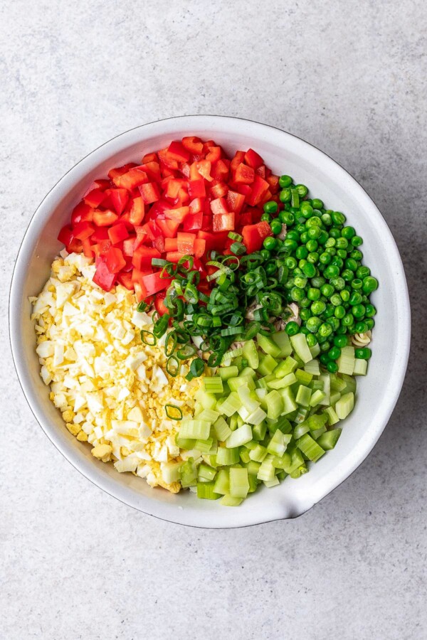 Diced peppers, celery, peas, and more added to a salad bowl.
