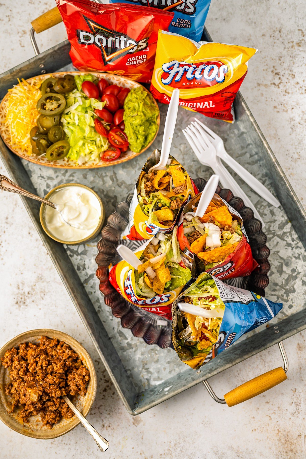 Overhead shot of four walking taco servings with spoons and toppings.