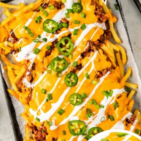 A baking sheet filled with chili cheese fries topped with sour cream, green onions and sliced jalapenos.