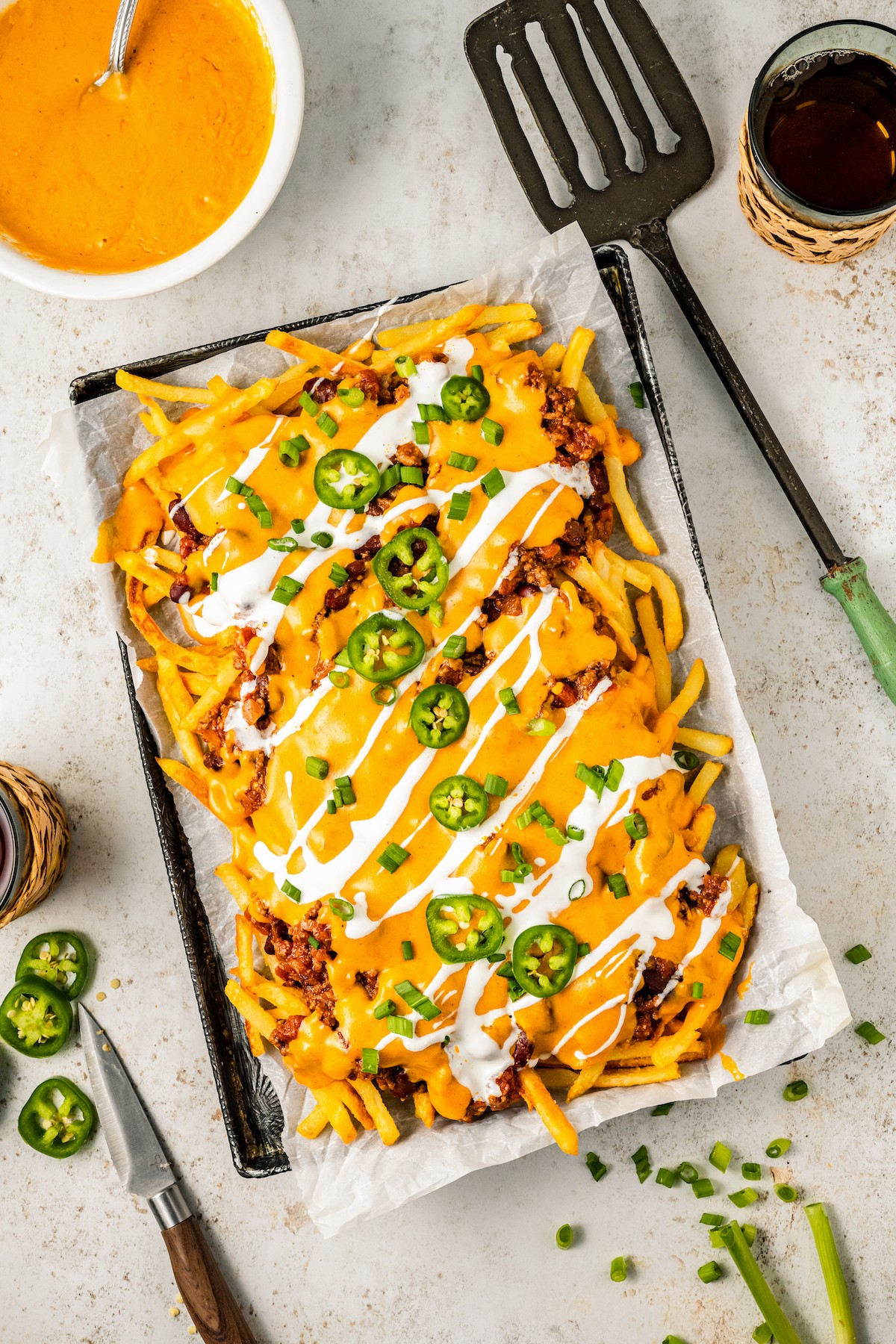 A sheet pan of fries topped with chili, cheese, sour cream, jalapeno, and green onion.
