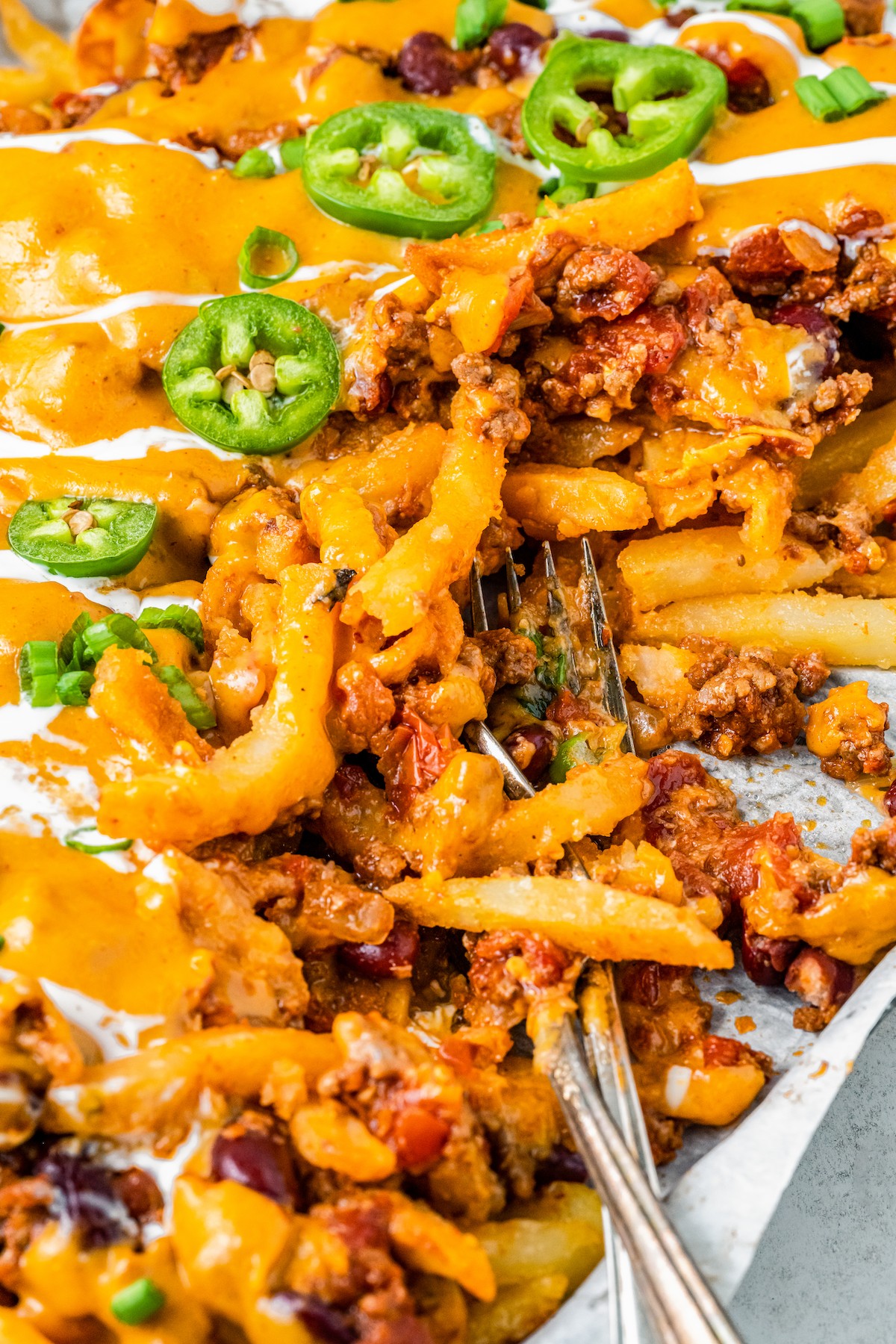 A fork resting in a batch of homemade cheese fries with chili.