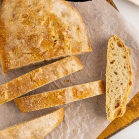 Ciabatta Bread sliced into pieces on a parchment paper lined cutting board.
