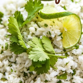 Cilantro and lime rice in a bowl with fresh cilantro and a lime wedge on top for garnish.
