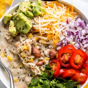 A bowl of slow cooker white chicken chili with all the toppings and a spoon in the bowl.