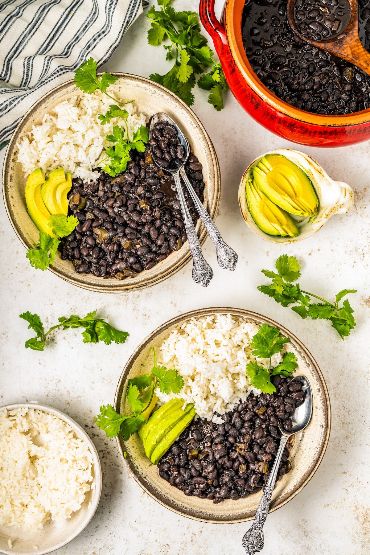 Two bowls of Cuban black beans recipe with avocado and rice. 