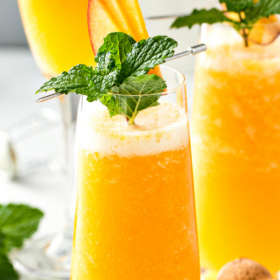 Peach Bellini in a Champagne flute with fresh mint and sliced peaches for garnish.